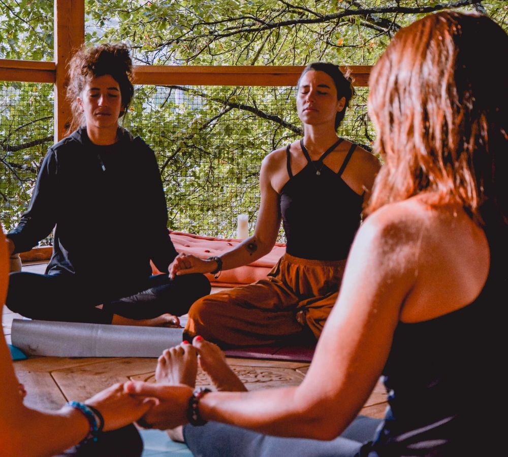 Une photo de Mélodie et d'autres femmes assises en position de méditation, se tenant toute la main pour illustrer les cercles de femmes.